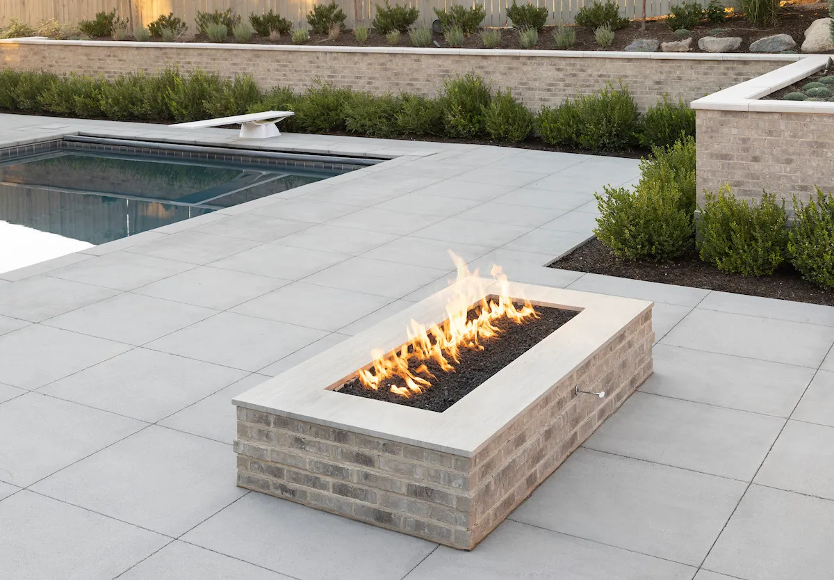 Swimming pool with lounge chairs, stone patio pavers, ornamental trees, lawn, and mountain views at sunrise.