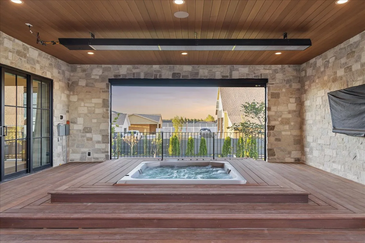 Hot tub integrated into wood deck beneath cedar ceiling with metal railings overlooking neighborhood at dusk.
